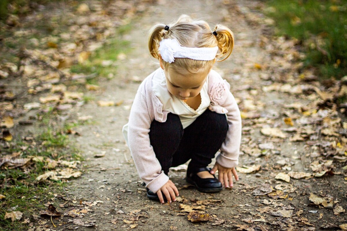 little girl playing with leaves in a dirt road