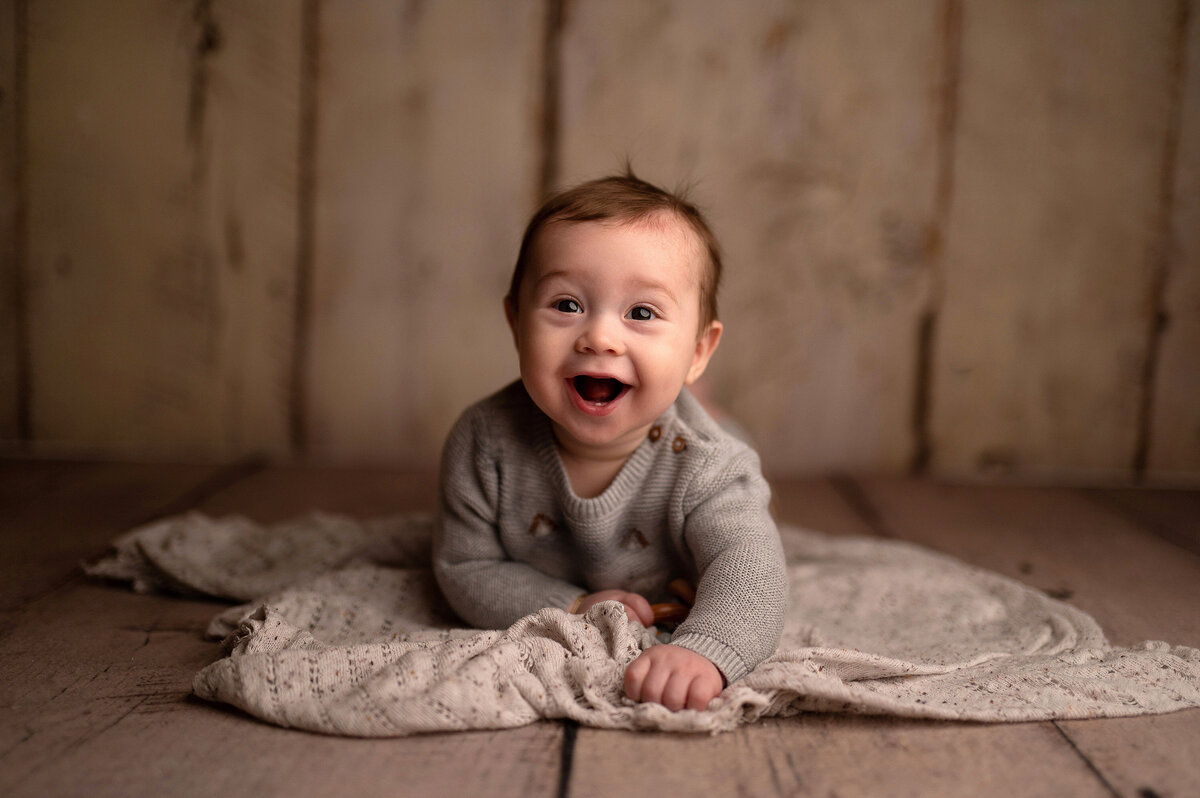 A baby boy crawls along the floor of our Waukesha portrait studio with is blankie while giving a HUGH smile.