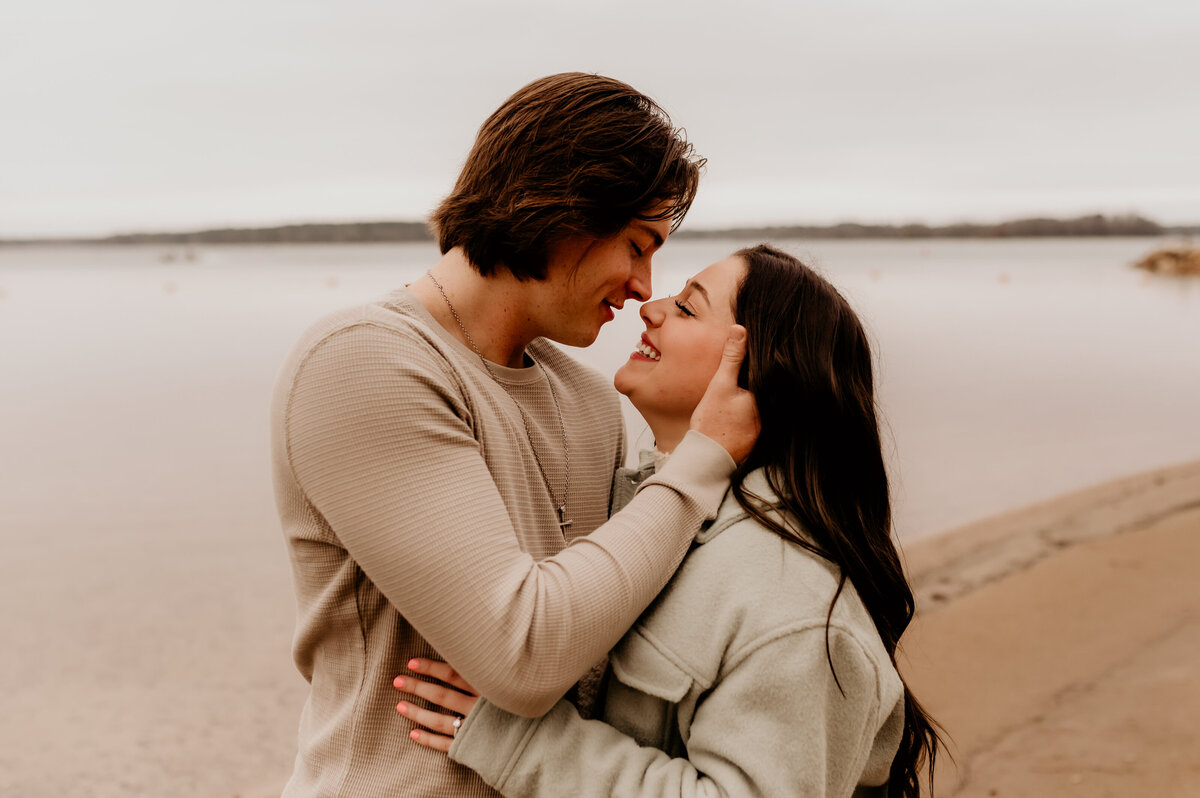 little rock engagement photographer captures man and woman embracing at a beach while the man holds the woman's hair and smiles down at her