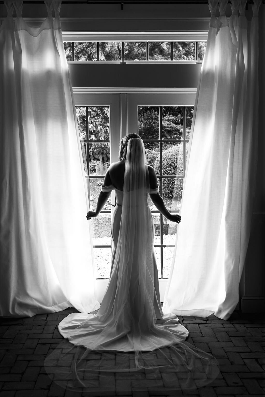 Bride looking out french doors while getting ready in the cottage at The Gardens at Uncanoonuc Mountain in Goffstown NH By Lisa Smith Photography