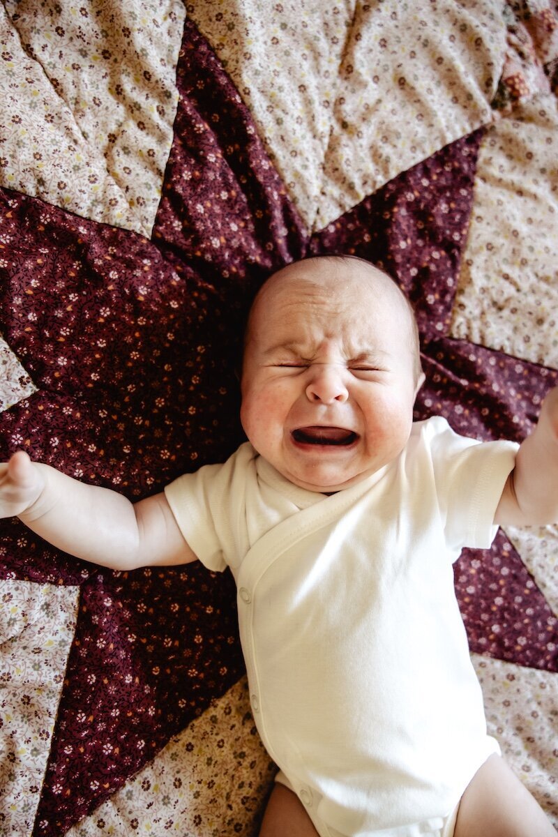 a newborn baby girl crying out on a handmade quilt