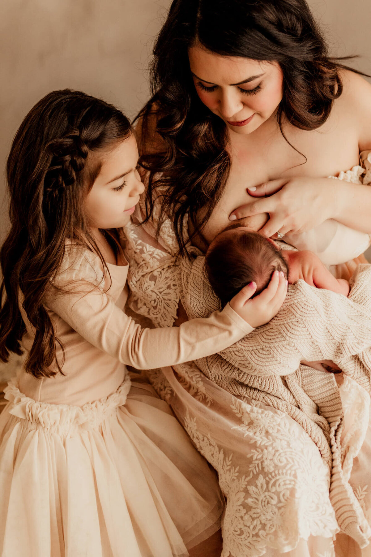Mother nurses her son while her older daughter strokes his hair.