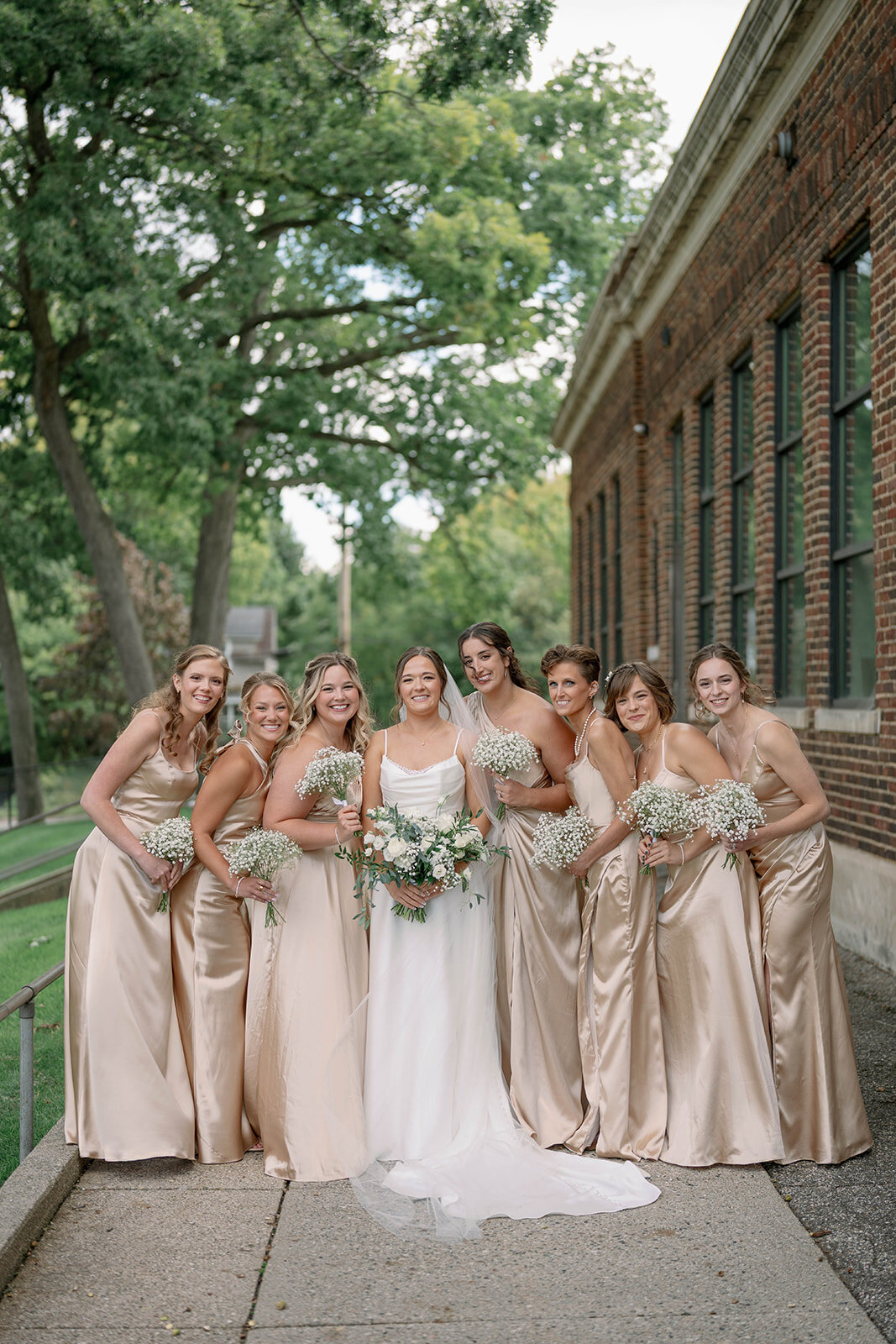 Bride and bridesmaids standing together for a portrait in champagne dresses at Leona Road Wedding Venue in Grand Rapids MI.