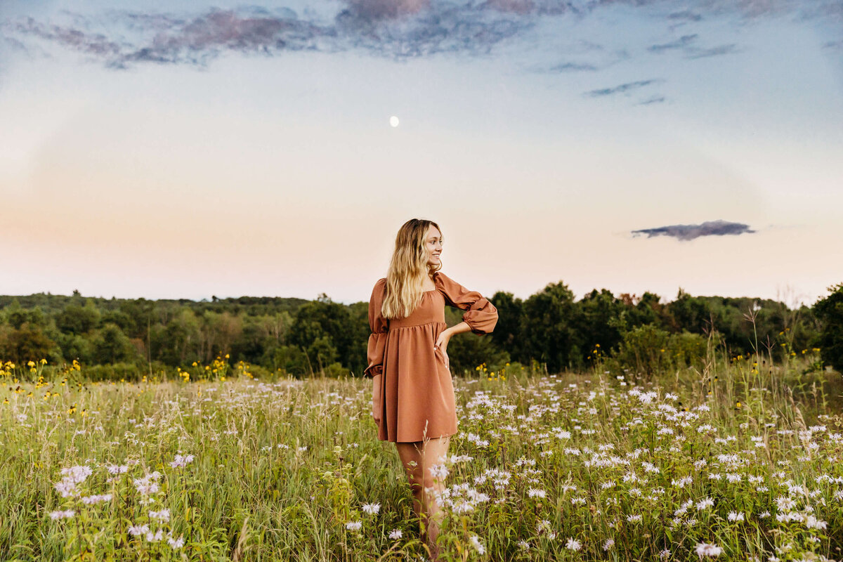 teen girl in orange dress standing in a field of wildflowers with the moon