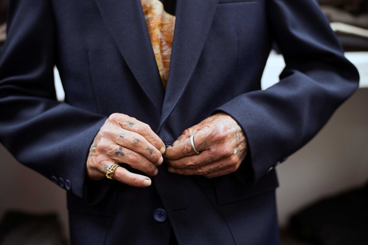 A detail shot of a man buttoning jacket with tattooed fingers.