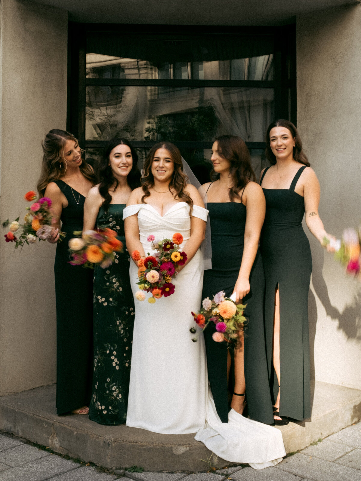 A bridal party holding colourful flowers laughs in front of a door in Old Montreal. 