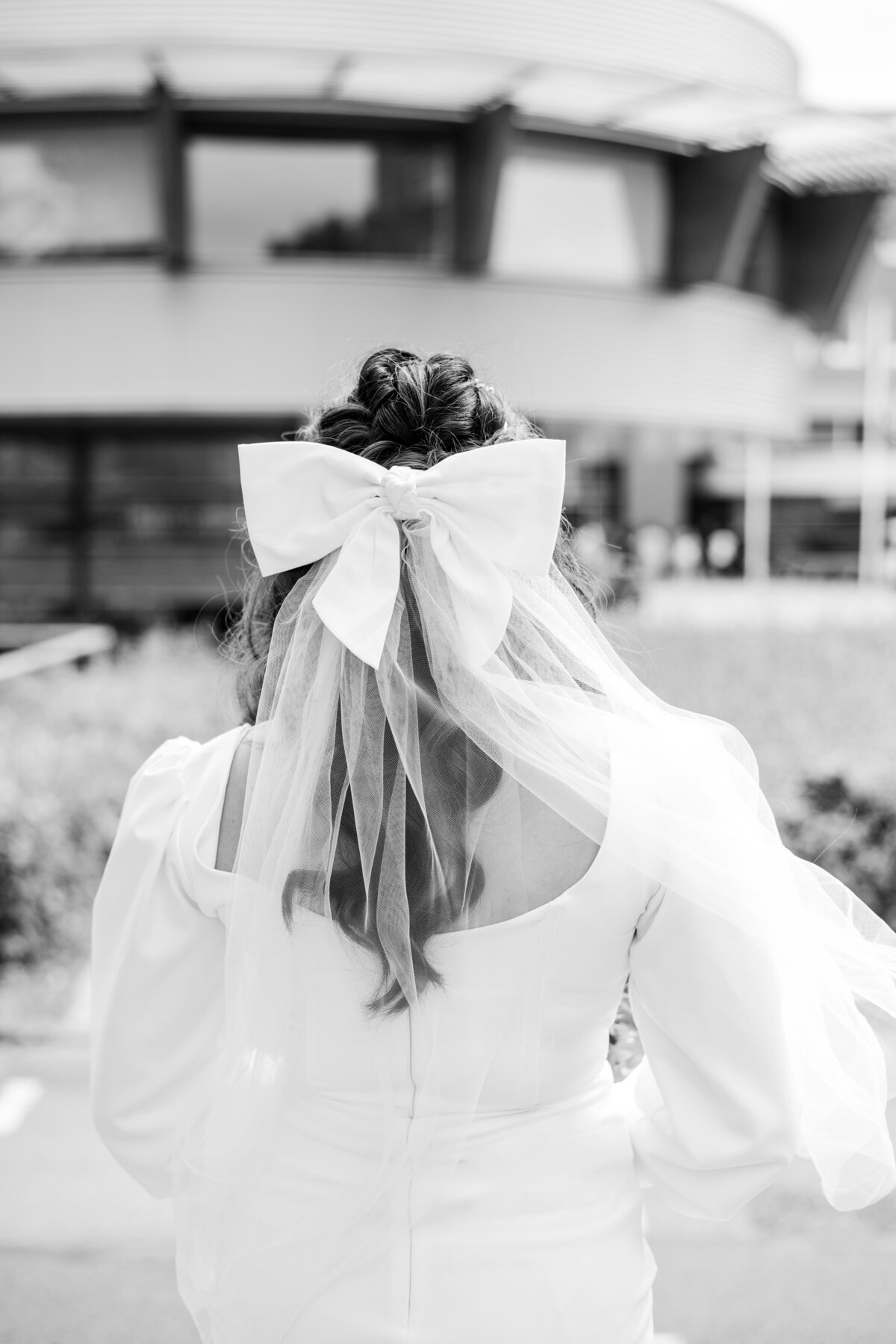 Black and white photo view of the back of bride Ronalyn showing her wedding dress detail, curled hair, veil, and oversized white bow in her hair