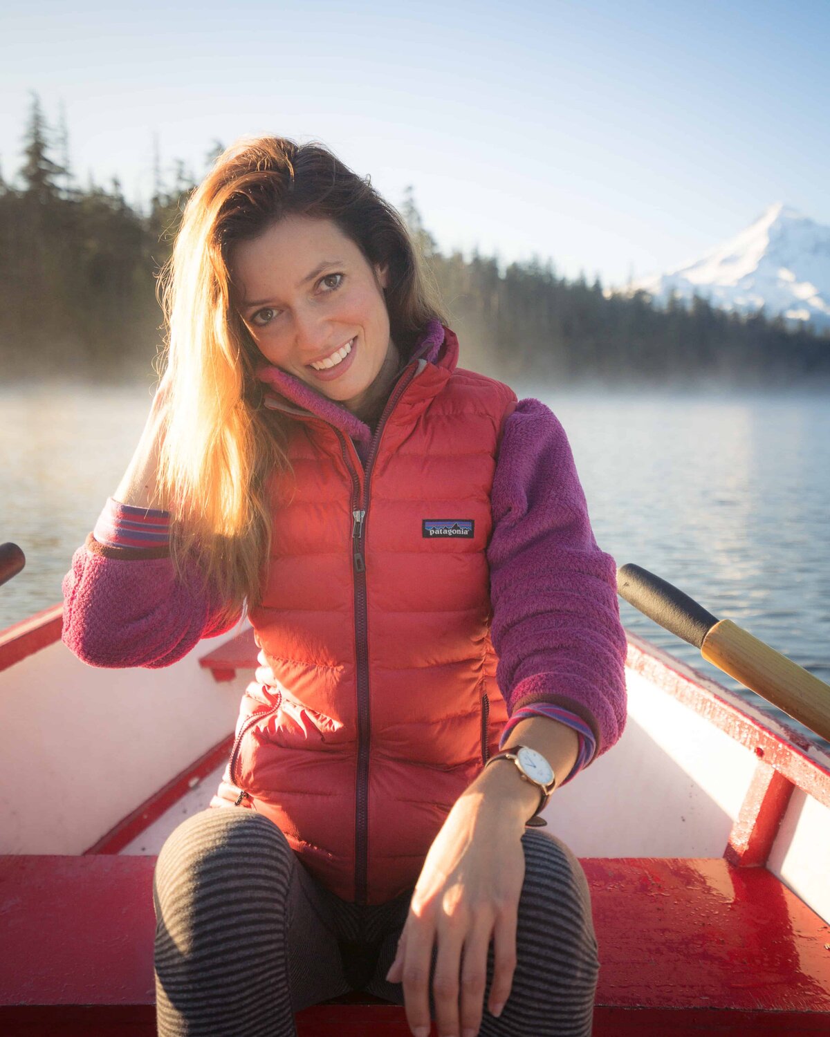 Woman in a red puffy vest sitting on a rowboat on a lake