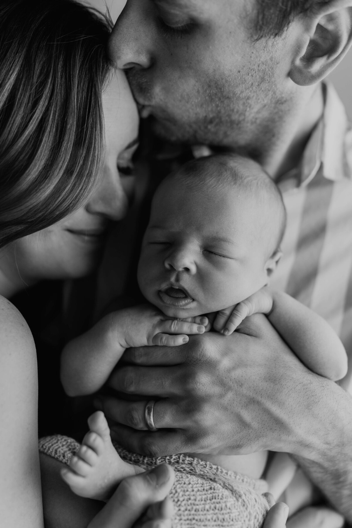 close up parents with their newborn as he sleeps in his dads arms during a newborn photography session in parker colorado
