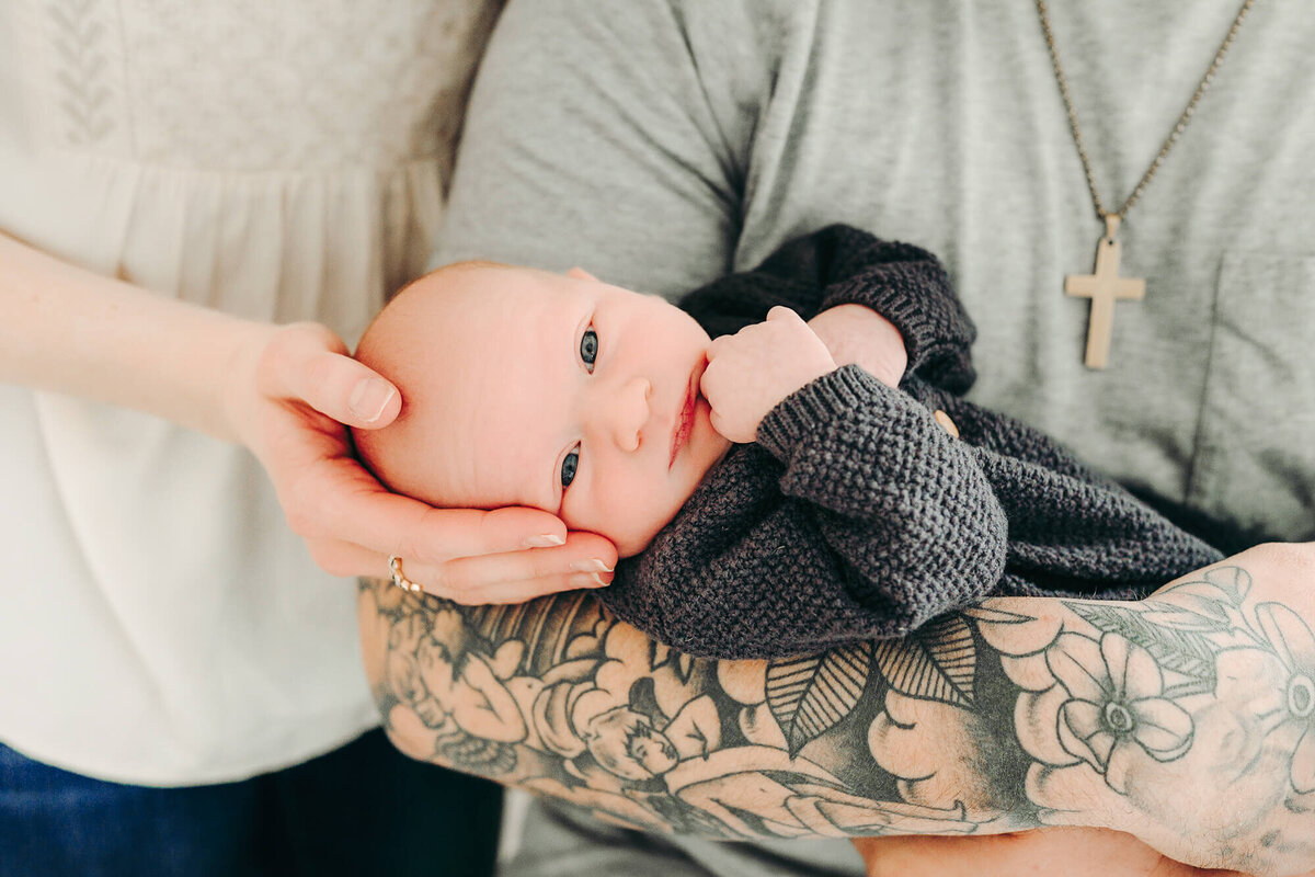 dad hold baby boy while mom cradles his head in her hands for newborn photos