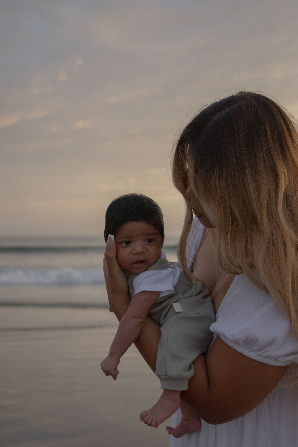 A mother holding her newborn baby by the ocean