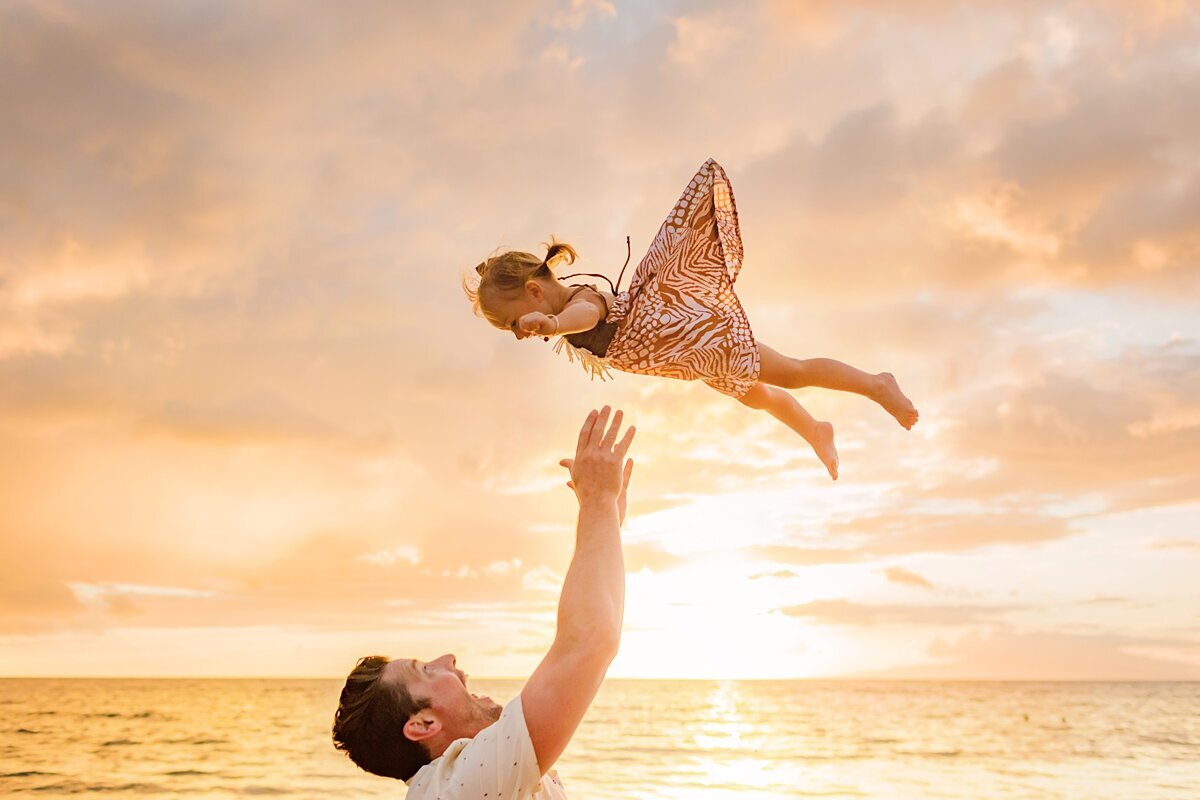 Dad throws his daughter in the air excitedly while being photographed on Maui by Love + Water Photography