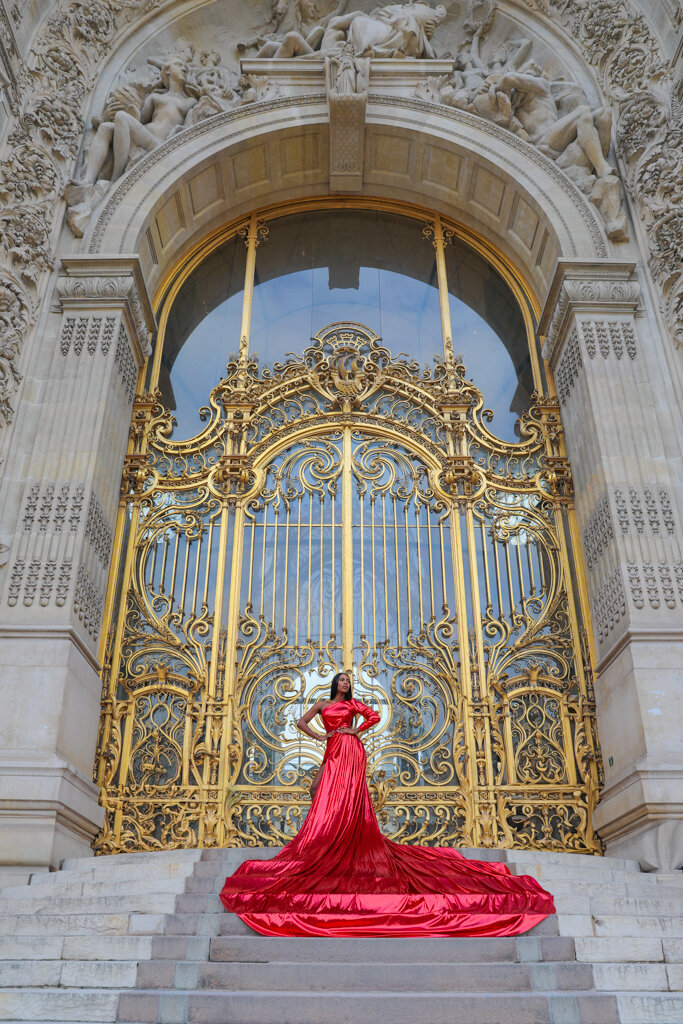 Elegant portrait session at Petit Palais featuring black woman in metallic red dress on golden gate