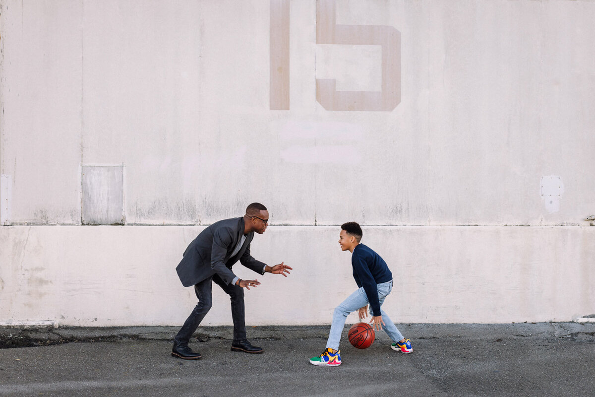 father and 11-year-old son playing basketball together in front of warehouse with number 15 on it at Alameda Naval Base