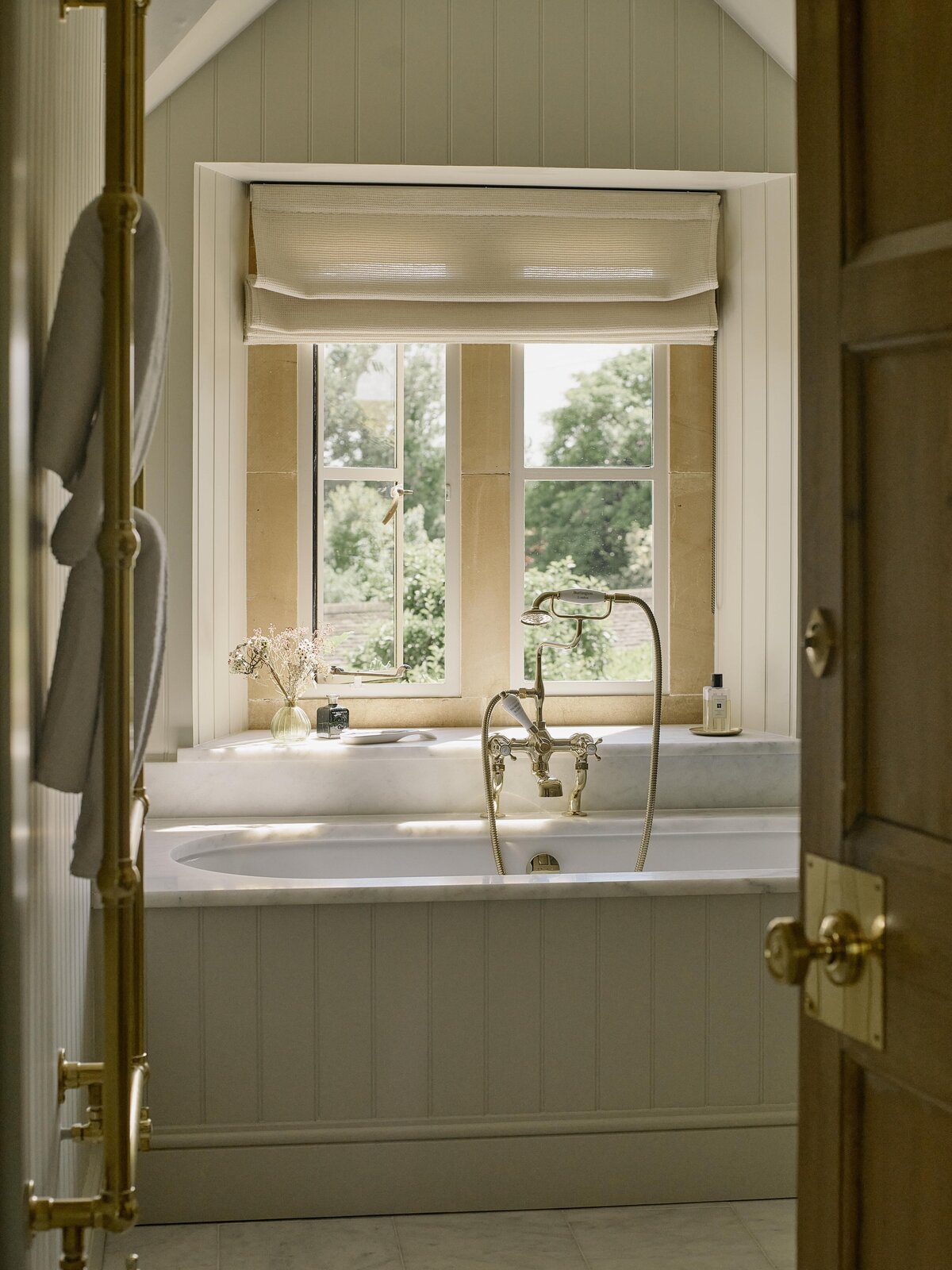 Sunny bathroom with panelled bath and brass hardware
