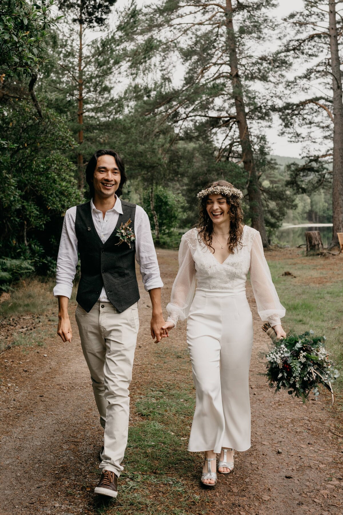 A newly married couple walk joyfully through the woodland grounds of Glen Tanar Ballroom after their wedding ceremony.