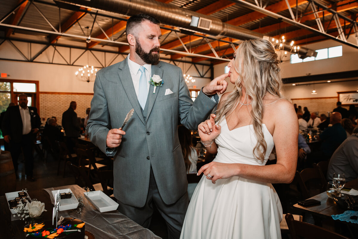 A groom lets his bride taste the cake off his finger while cutting it