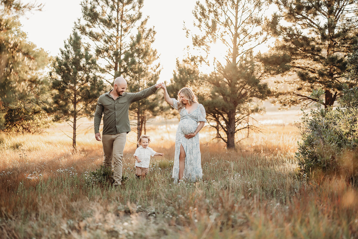 mom and dad holding hands through a field while son runs under hands