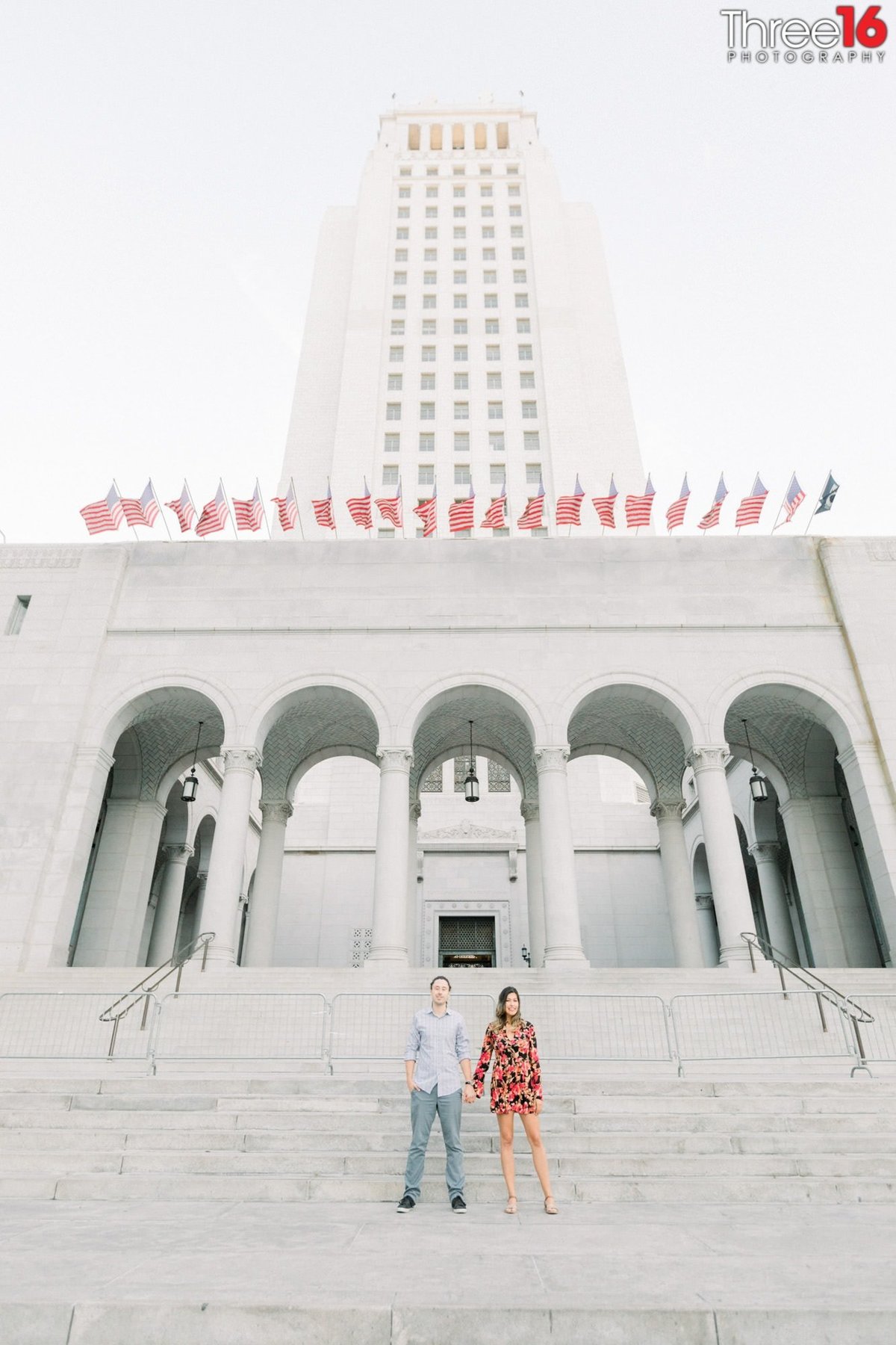 Engaged couple hold hands on the steps of the Los Angeles City Hall