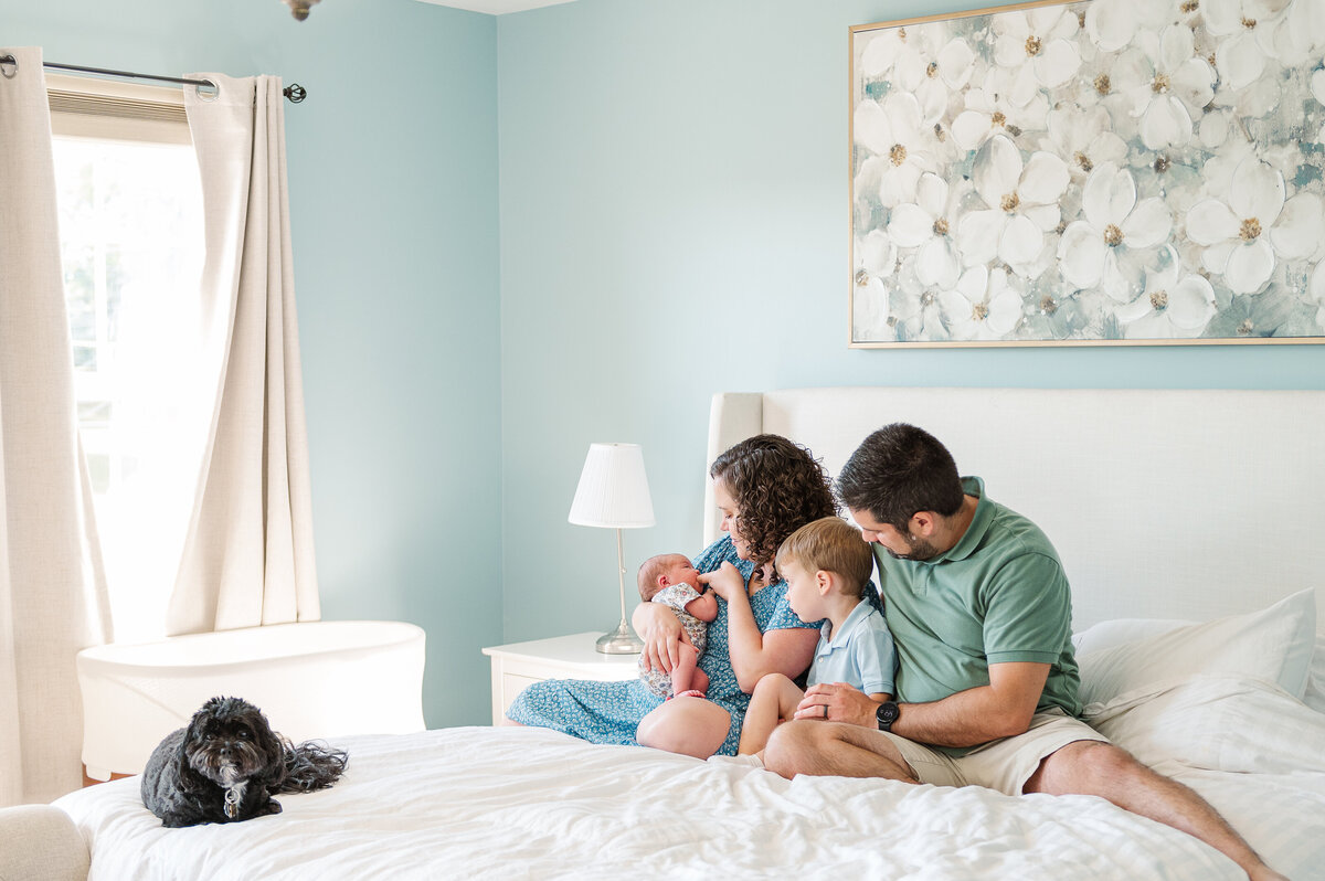 Family sitting together on a white bed with blue walls with their newborn baby and their puppy dog by Lancaster pa photographer