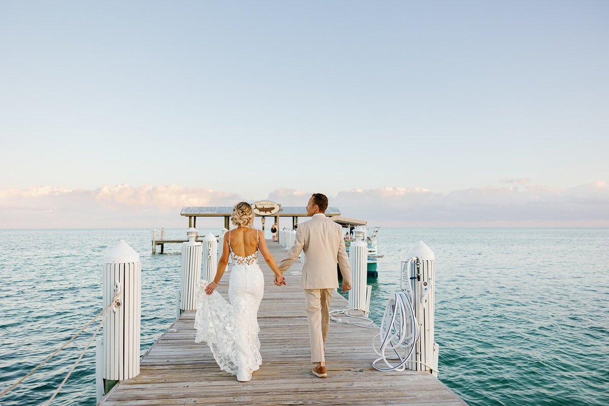 Ashley and Hunter hold hands, strolling on a picturesque pier with the ocean stretching behind them.