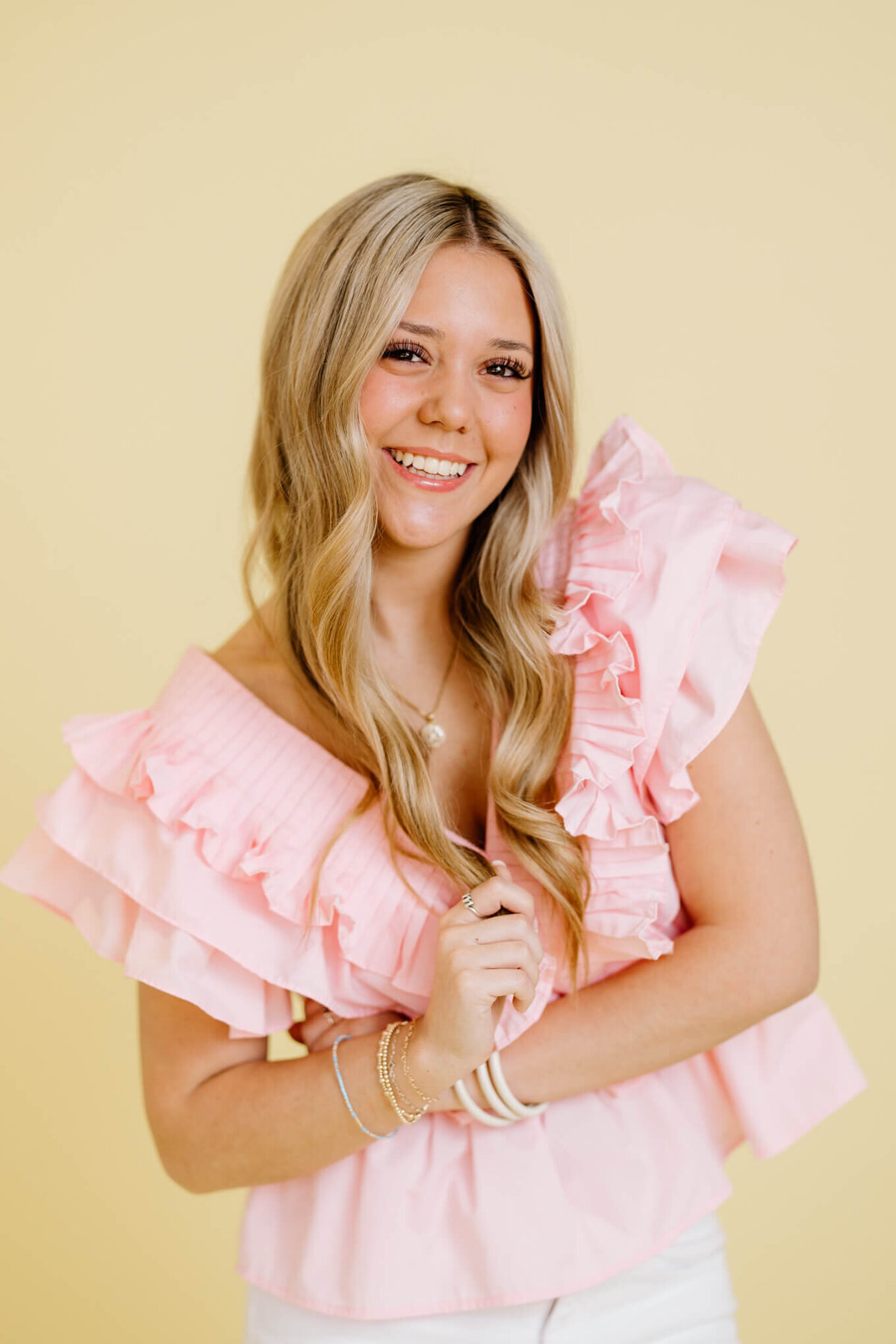 Candid and fun headshot for TCU student in light pink top, white jeans, and light yellow background