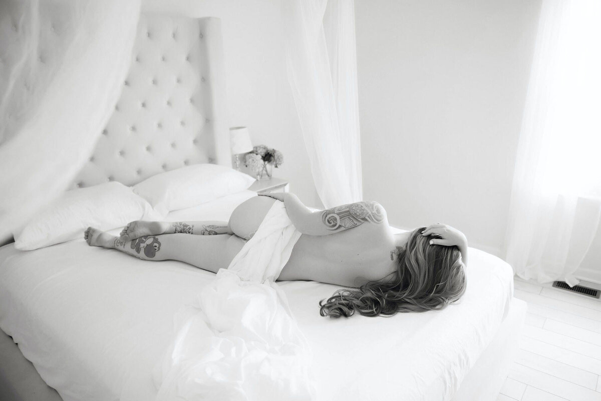 Woman-laying-on-white-sheets-in-classy-boudoir-photoshoot
