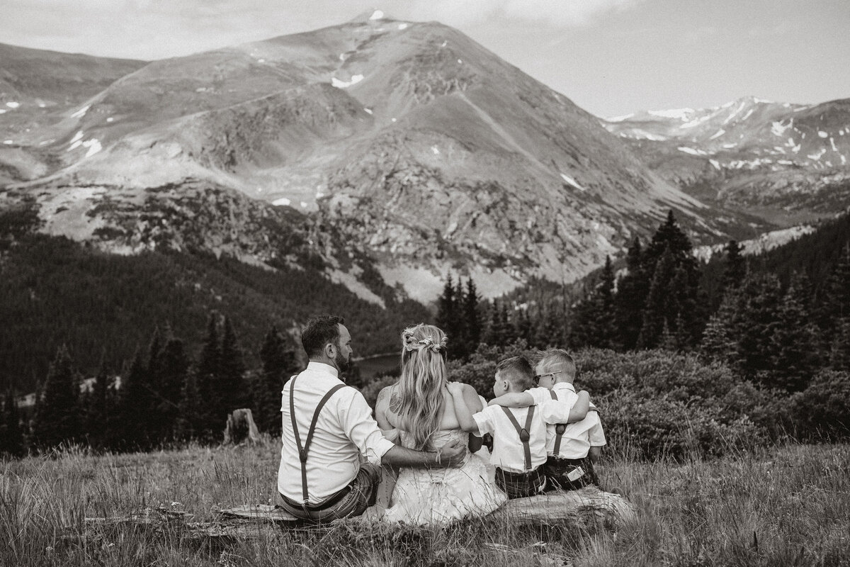 Family of four sits together with arms linked, facing Breckenridge mountains after intimate wedding ceremony.