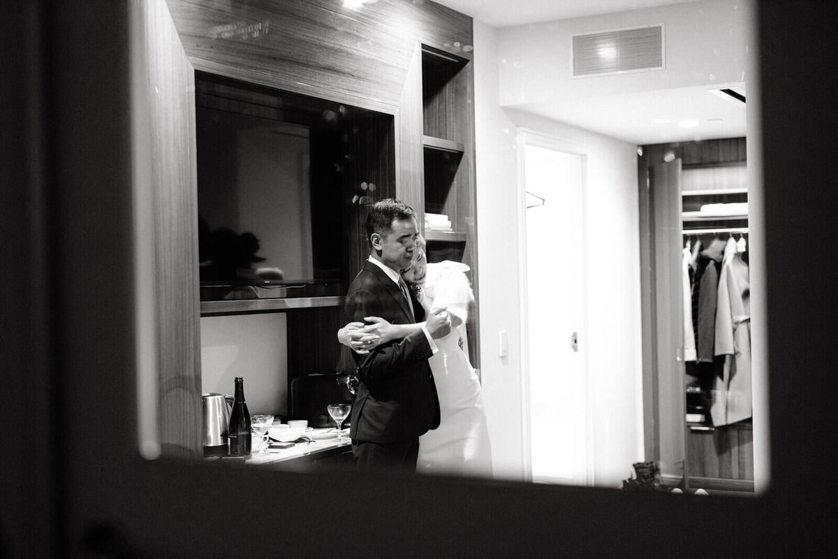 A reflection of the bride, hugging the groom, in a mirror inside of a hotel room.