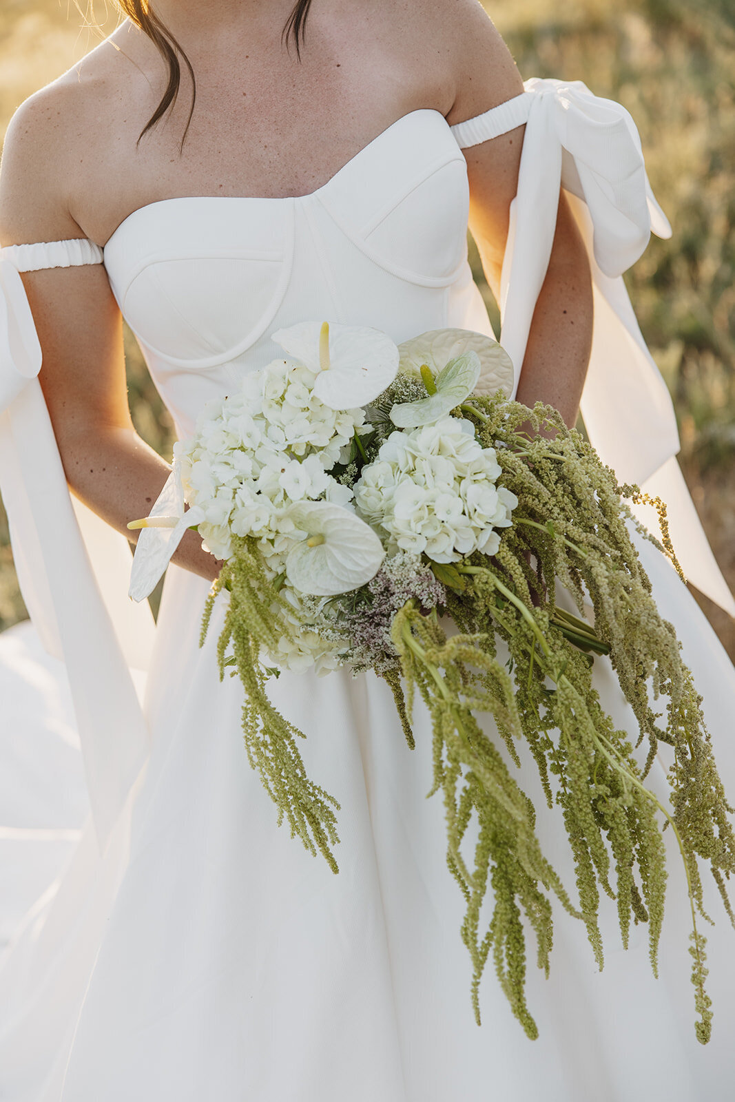 Intimate mountain wedding photo: close-up of a bride holding a simple, elegant white bouquet, highlighting natural beauty and grace.