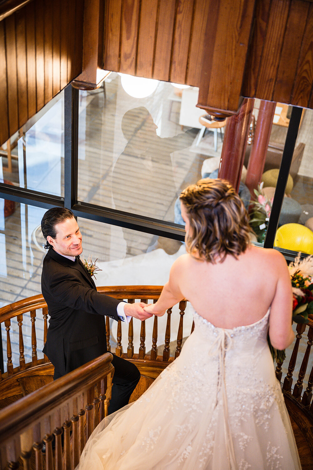 A groom reacts warmly to seeing his partner during their first look and reaches for her hand on an antique stairwell in the Fire Station One hotel in Roanoke, Virginia.