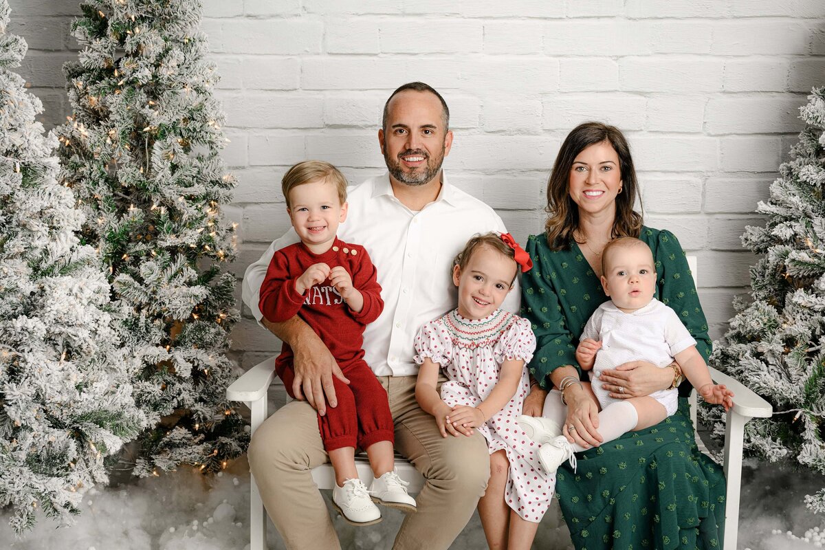family of 5 sits on a bench during holiday mini photo session wearing holiday colors of red and green