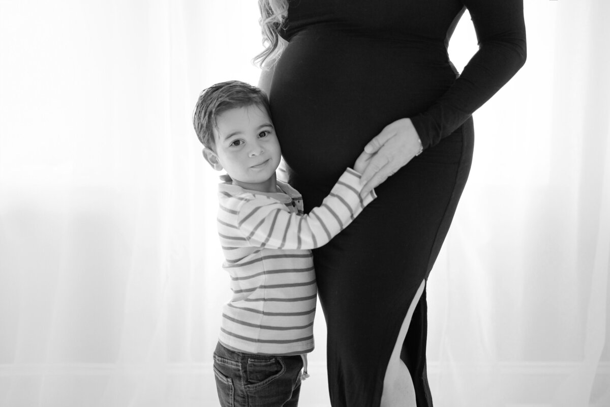 Elegant maternity portrait of Christina and her son standing by window with natural light pouring in during Tampa studio session