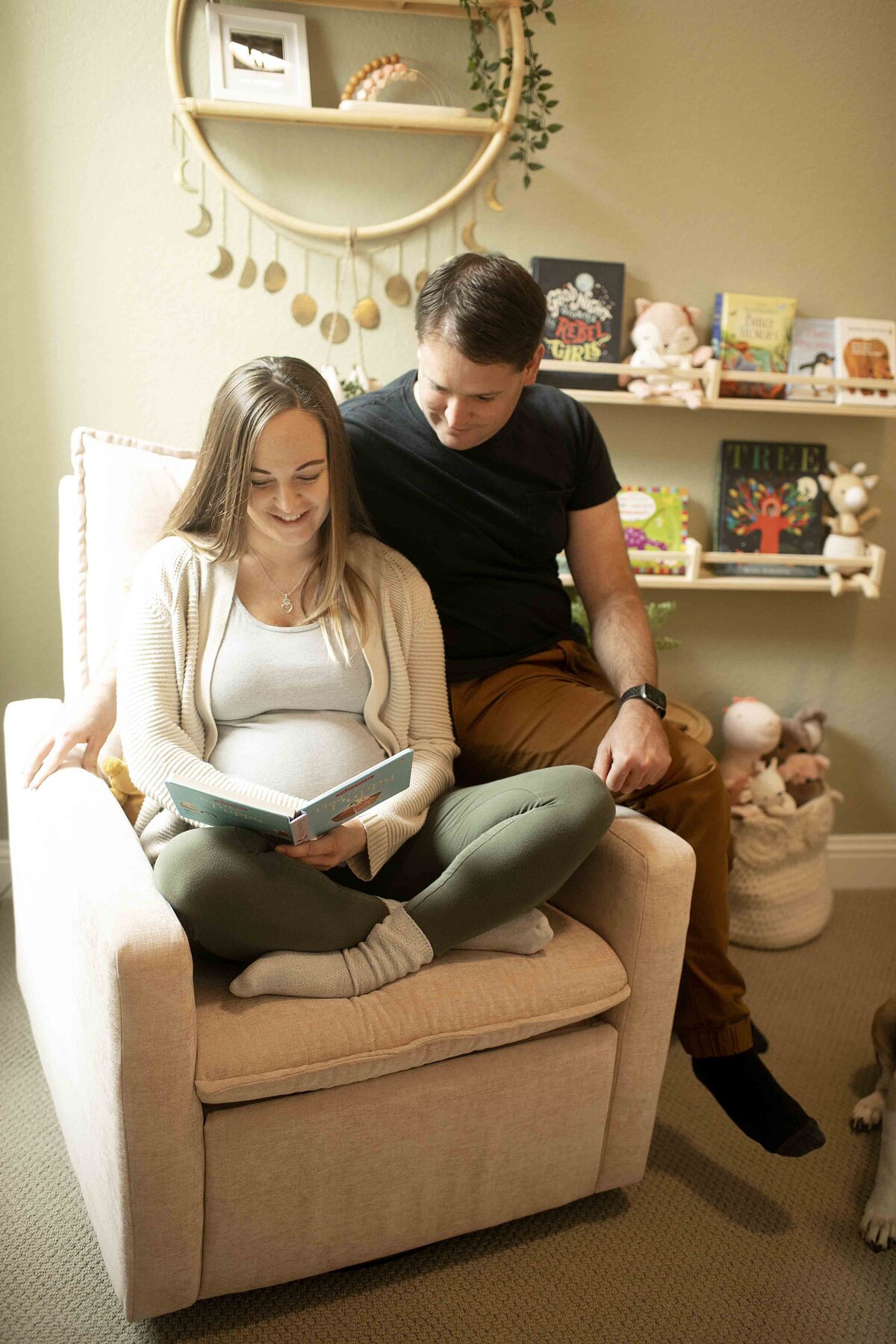 A serene maternity moment of mom in the nursery, sitting comfortably in a chair, reading a book to her baby with a calm and loving smile, captured by Chunky Monkey Photography.