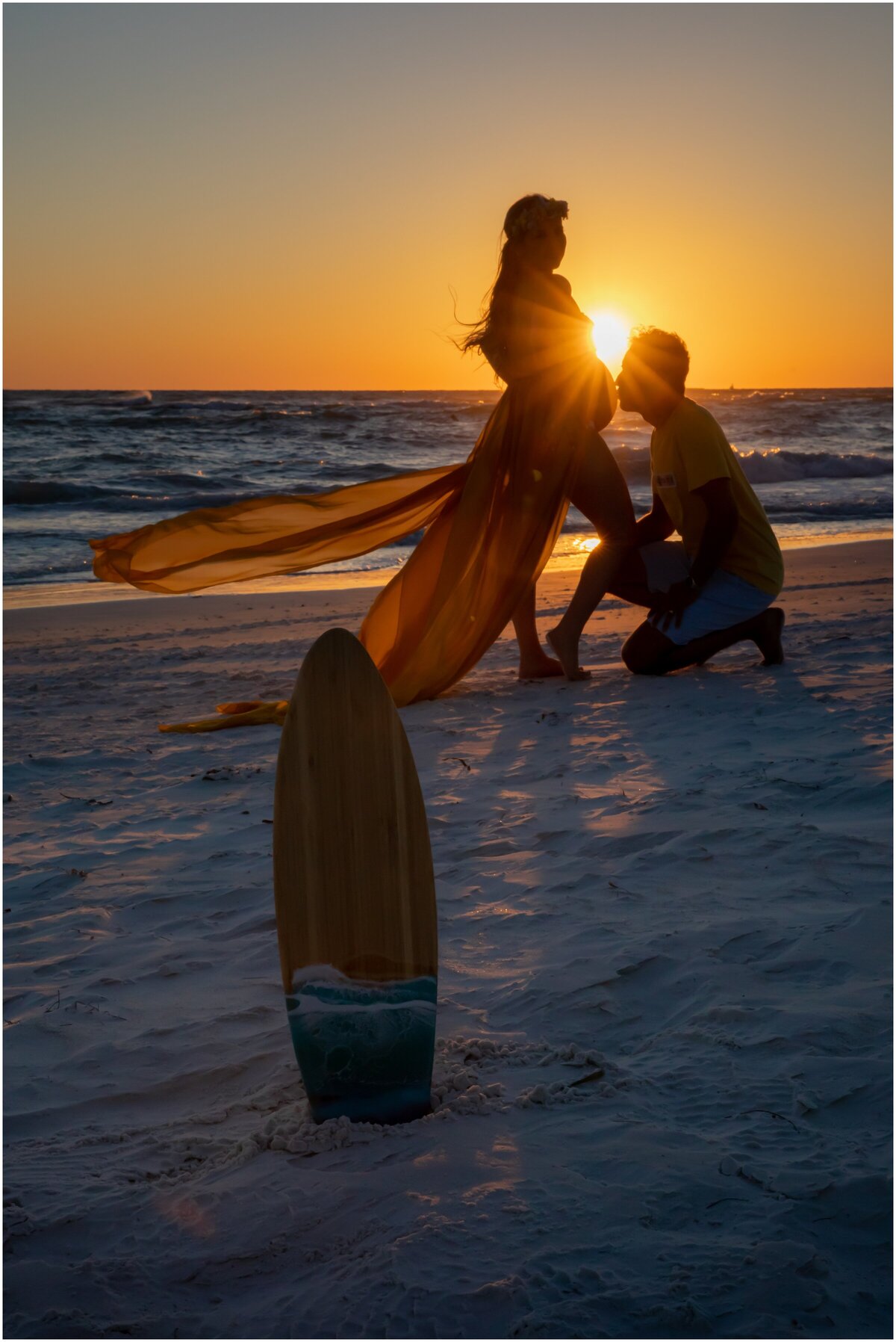 A silhouette against the sunset background of a pregnant women with husband kissing the belly