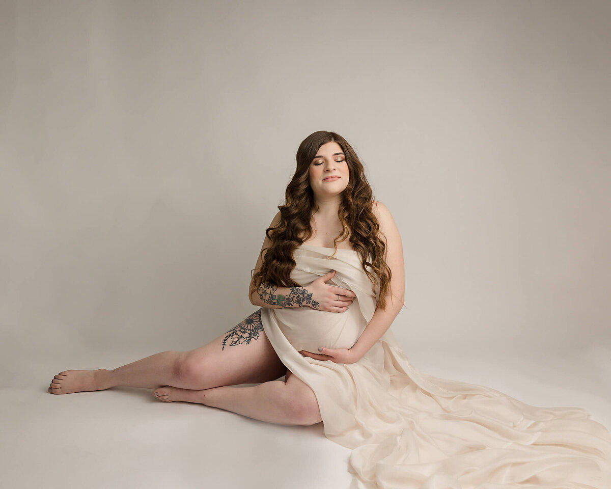 editorial portrait of pregnant woman with silk covering belly sitting down