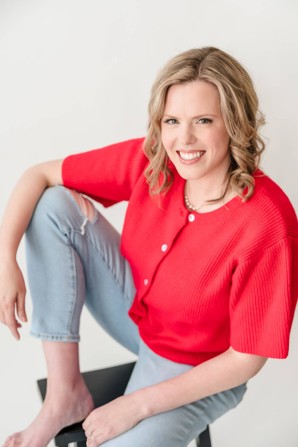 Close-up of smiling female entrepreneur in red knit top and light ripped jeans.