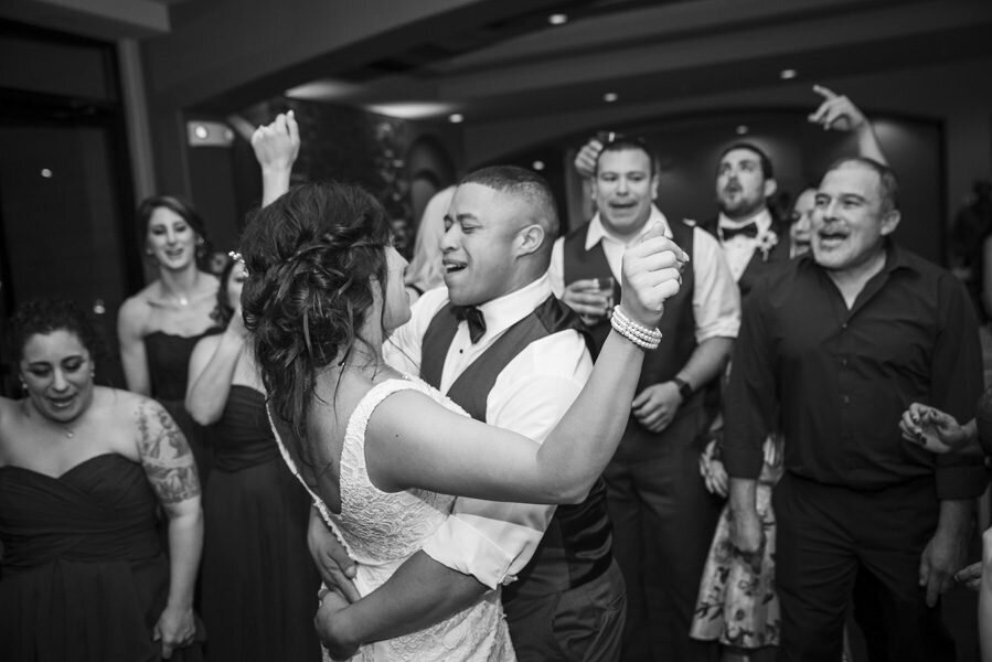 A bride and groom embrace in a hug as they share a fun dance surrounded by guests at their wedding reception.