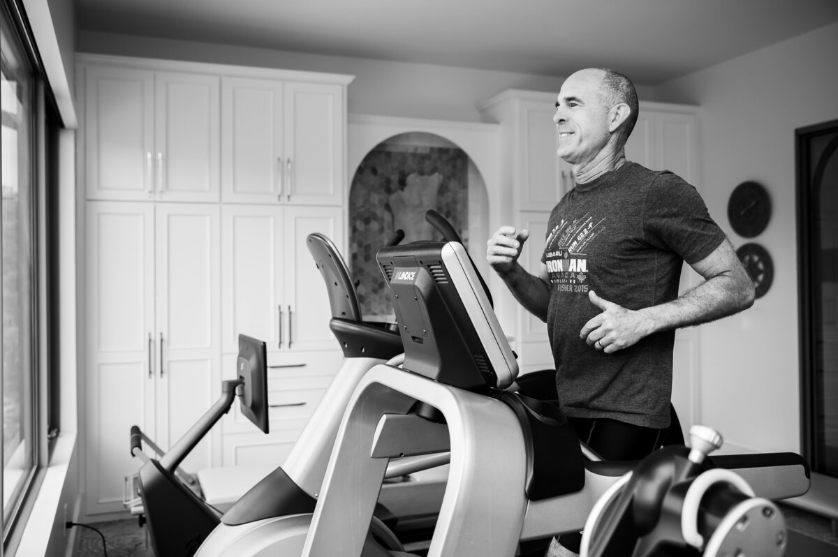 Black and white photo of a middle aged man running on a treadmill wearing a grey shirt