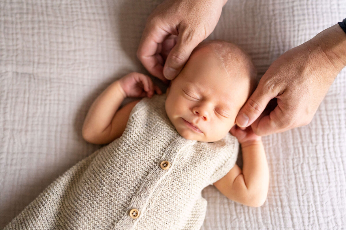 Newborn baby in tan knit outfit while father touches his face