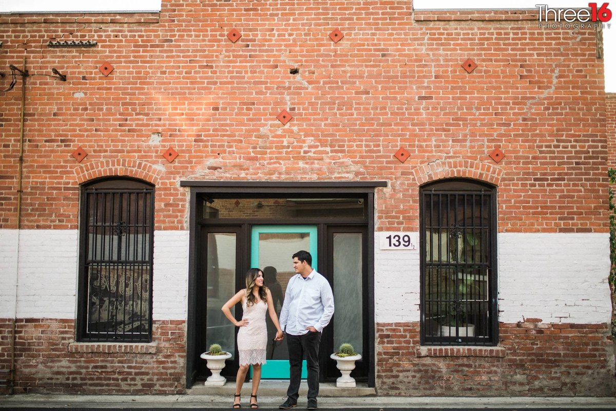 Engaged couple hold hands standing in front of an old warehouse building in Old Towne Orange