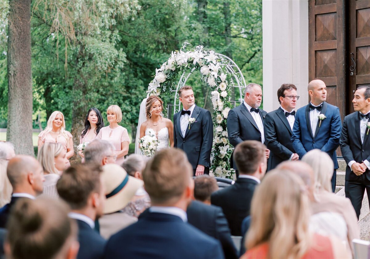 Destination Wedding Photographer Anna Lundgren - helloalora Rånäs Slott chateau wedding in Sweden outdoor ceremony with flower wedding arch wedding party and guests wedding smoking wedding