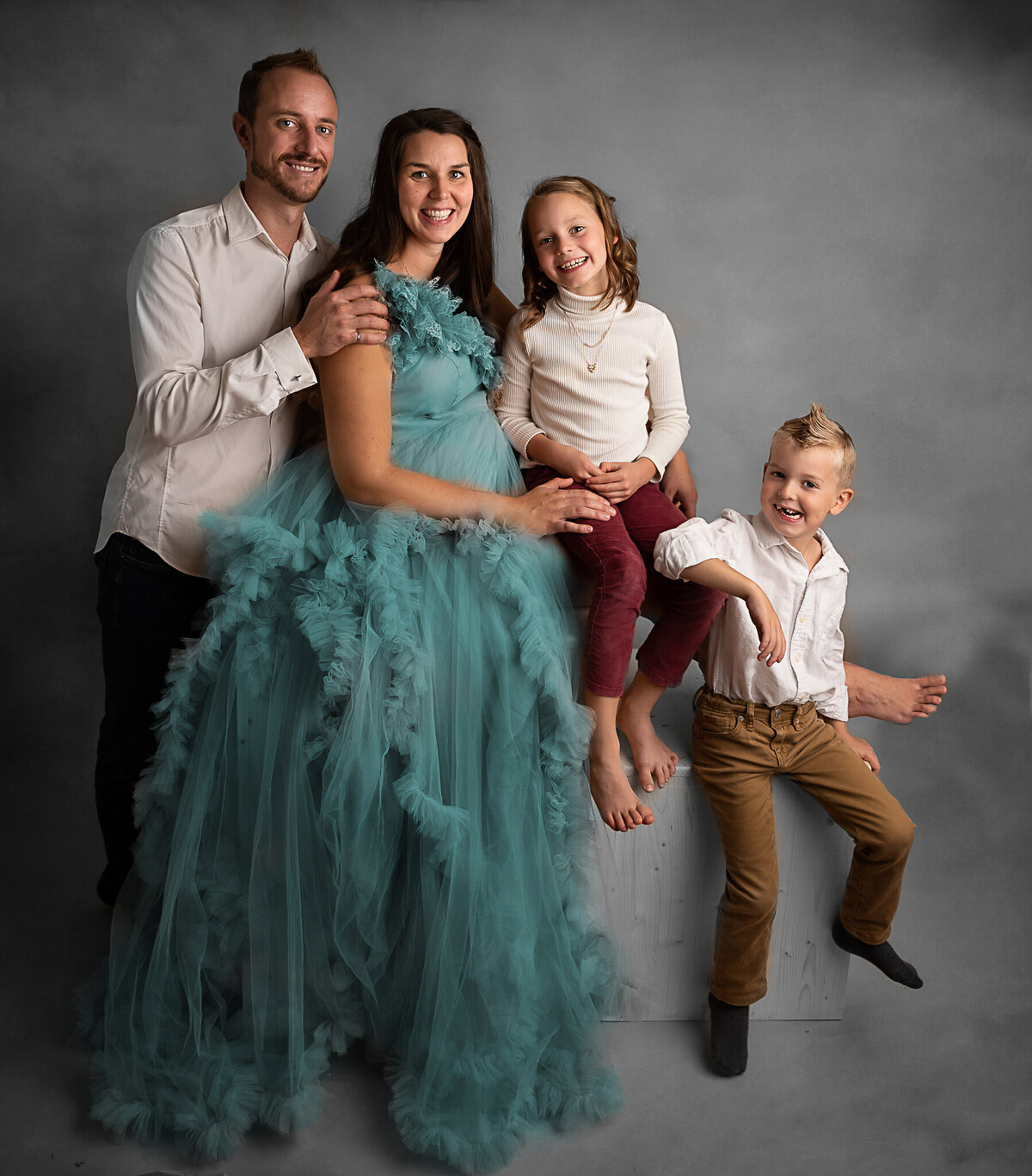 Maternity portrait session with kids and husband on a grey textured background.