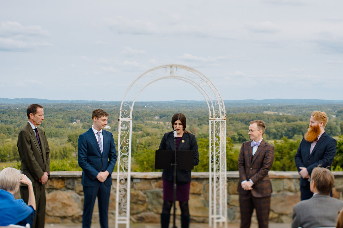 Five people standing up in front of the aisle at a wedding that overlooks a wooded area.
