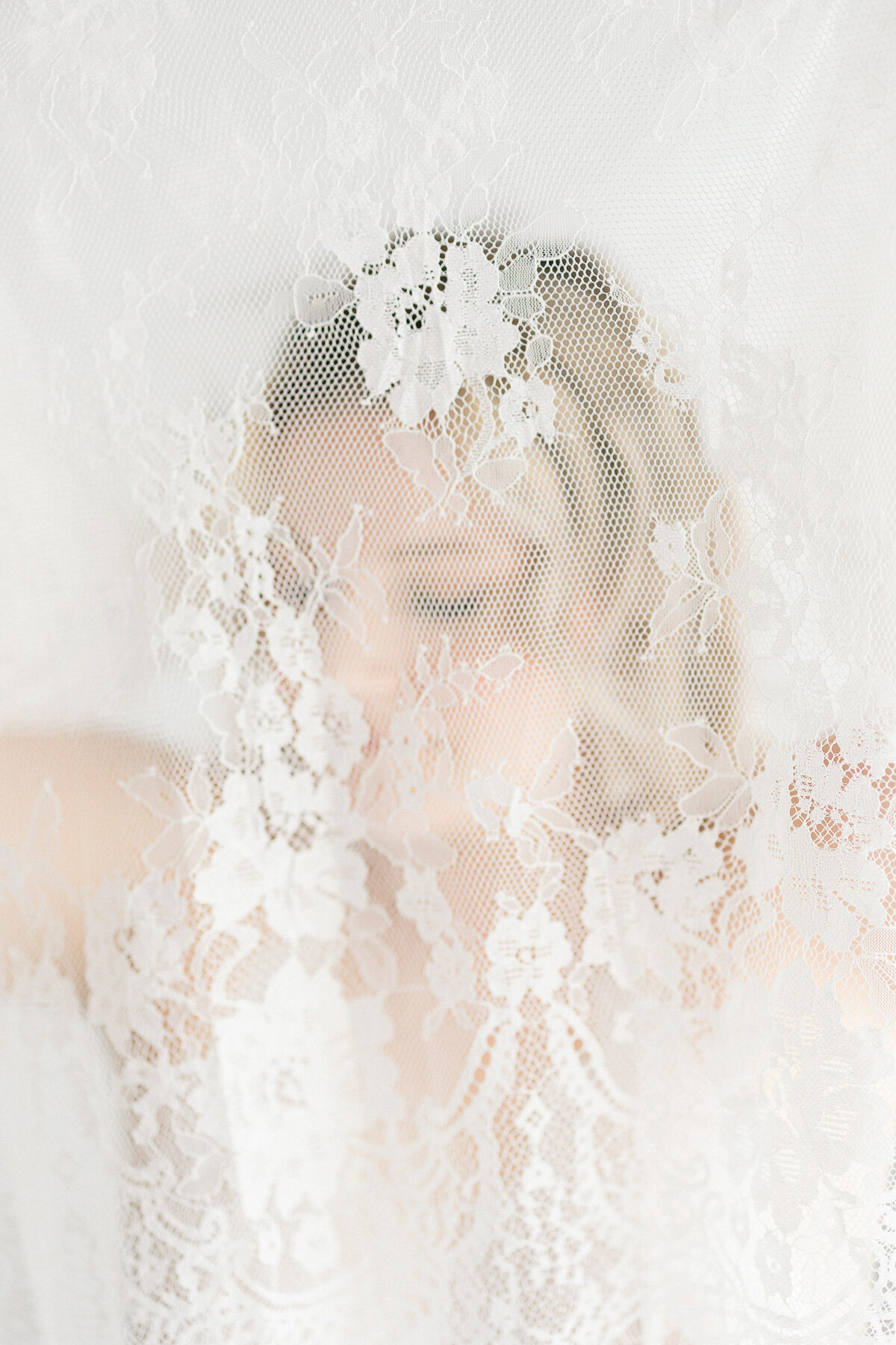 A woman looks down behind white lace during an Indianapolis boudoir photography session.