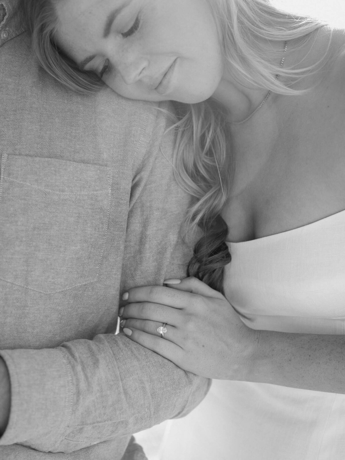Bride leaning on her groom's shoulder showcasing her engagement ring.