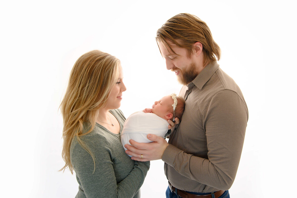 mom and dad holding baby wrapped in white for their family newborn photos