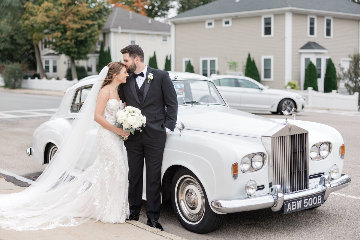 Newly weds share a kiss by a vintage Rolls Royce