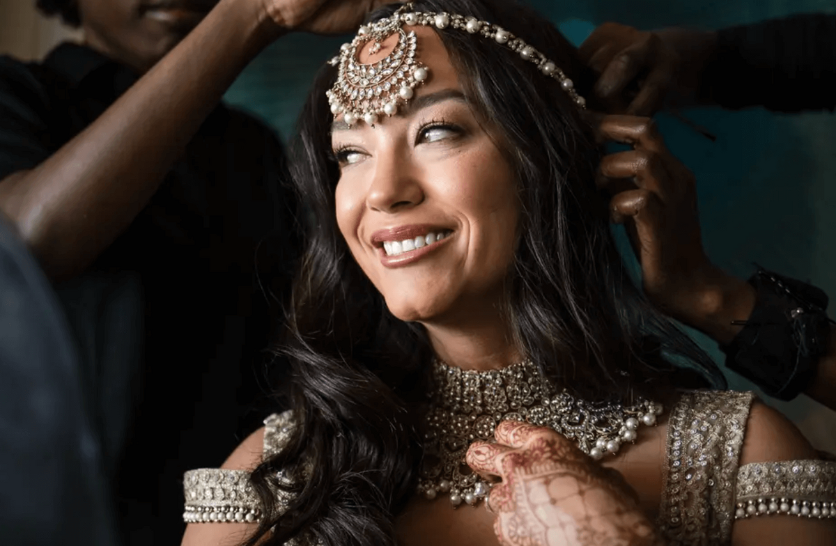 Bride smiles as final touches are made to her jewelry and makeup, styled by Mistique Makeup for her wedding in Austin