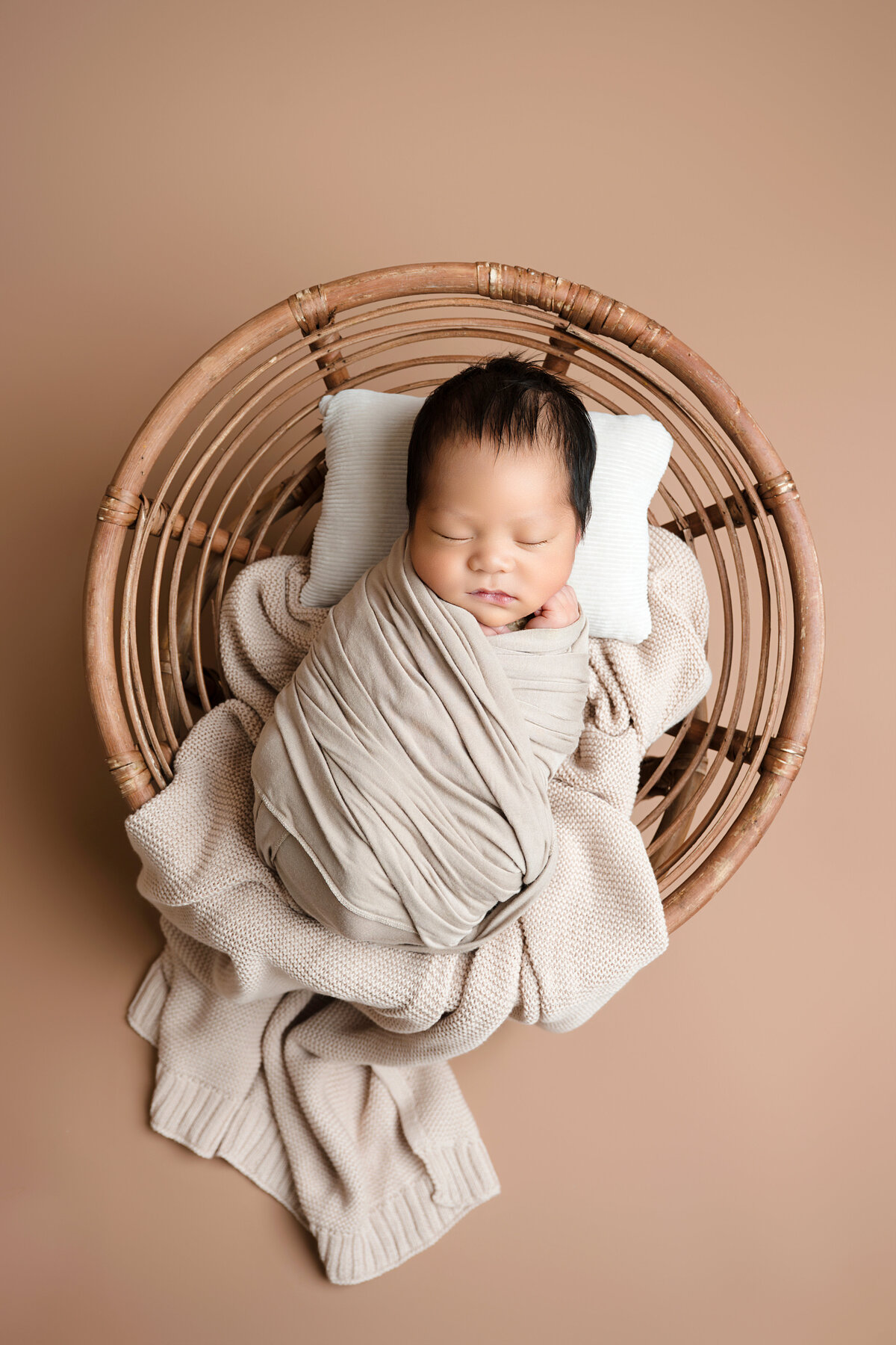 baby boy sleeping in a round wicker basket and wrapped in neutral blankets and wraps